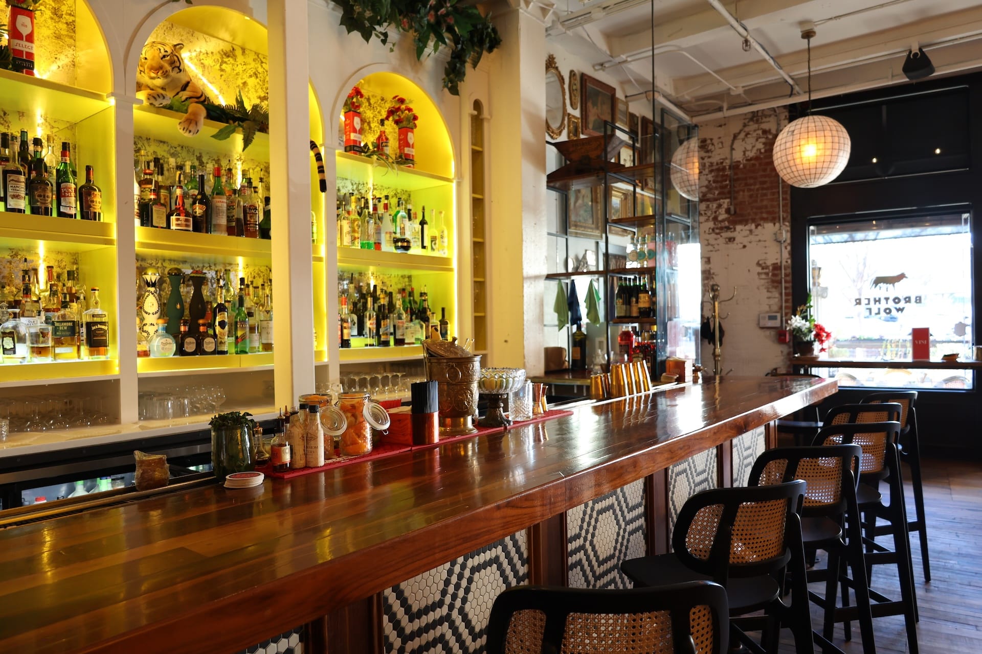 Interior bar at Brother Wolf aperitivo bar in Knoxville with backlit arched bottle shelves, wood bar top, mosaic tile, and exposed brick walls
